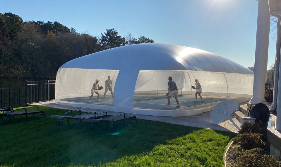 Backyard pickleball court covered by a white air-supported dome