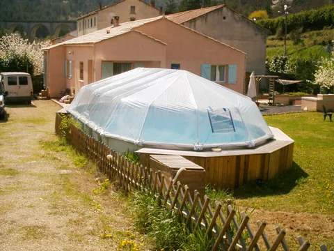 Clear vinyl Fabrico Sun Dome over an above-ground pool with a surrounding wood deck