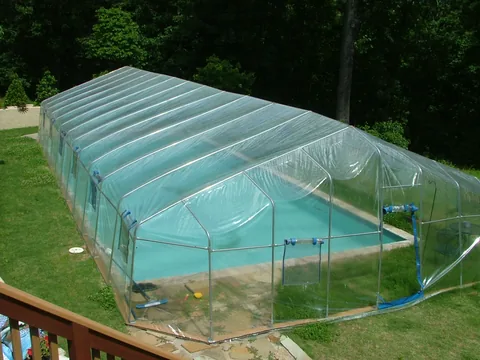 Rectangular clear vinyl Fabrico enclosure around an inground pool, with the frame and entry visible