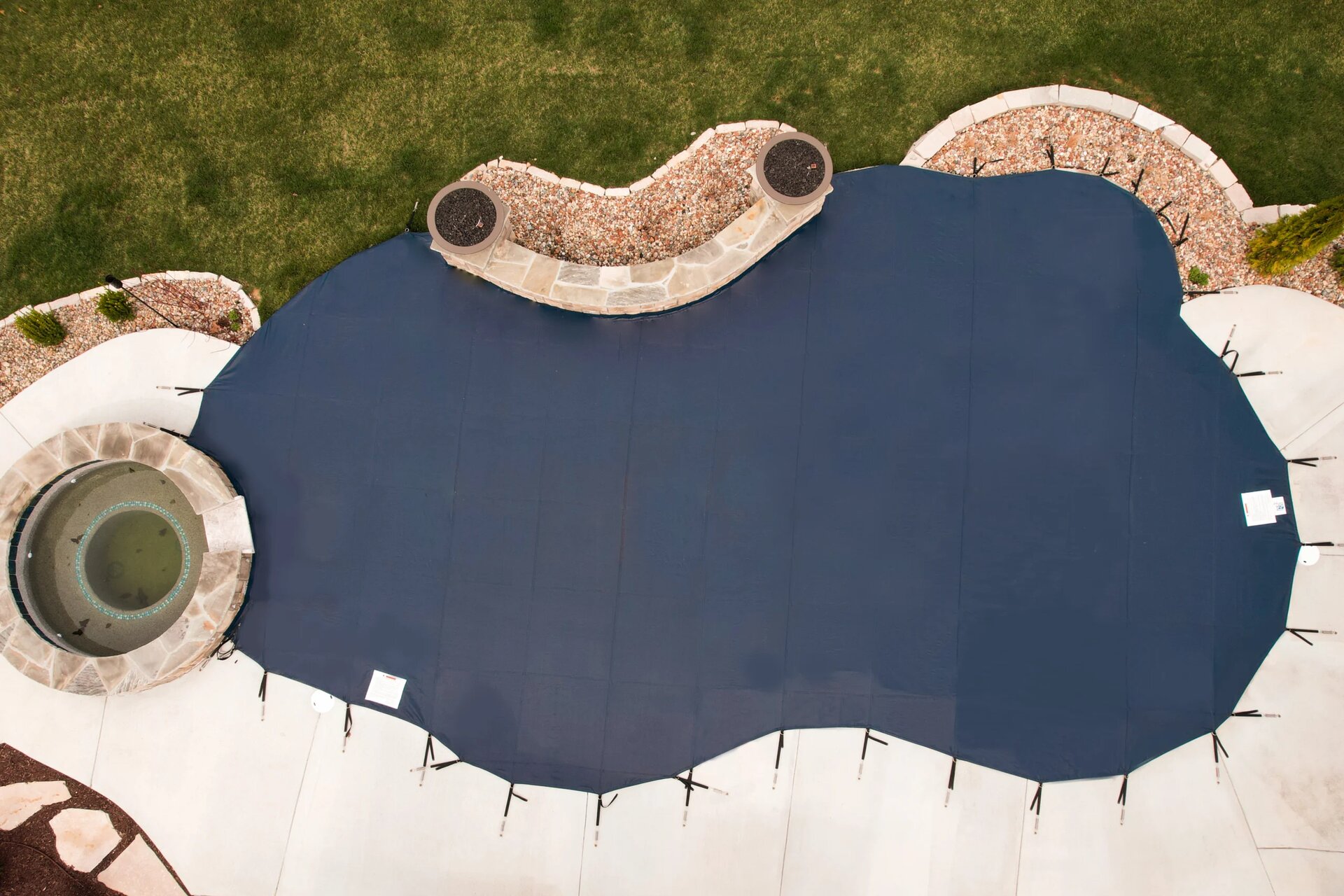 Custom blue Anchor safety pool cover fitted around a spa and landscaped pool deck