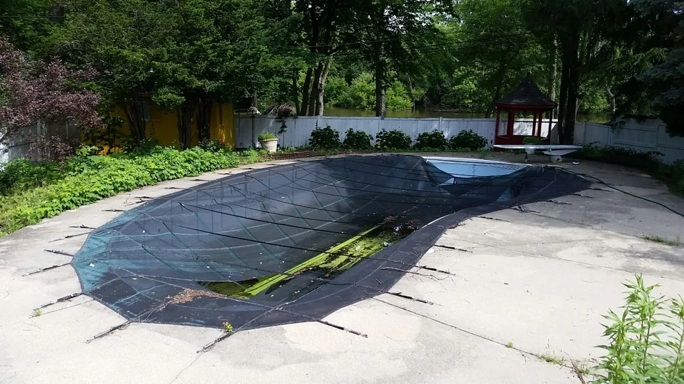 Damaged black pool cover with torn material sagging into the water