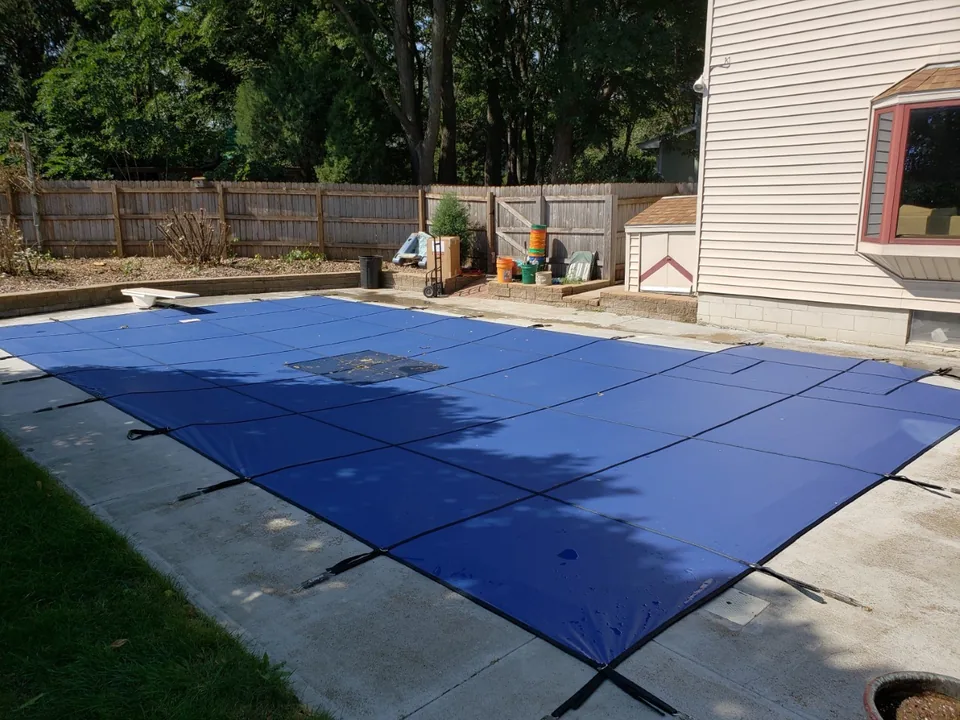Blue solid vinyl pool cover with a rectangular mesh drain panel in the center