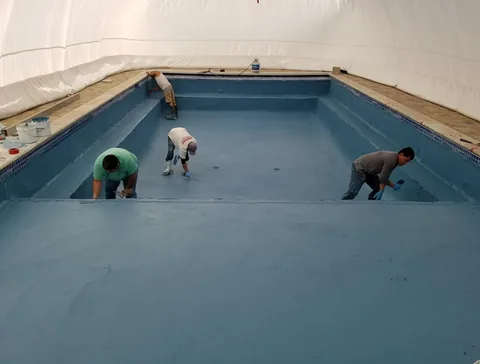 Workers plastering a pool inside an inflated construction dome