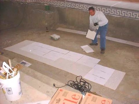 Worker laying out pool tile inside an unfinished pool beneath a dome