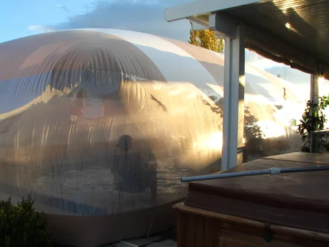 Transparent side wall of a striped pool dome beside the patio