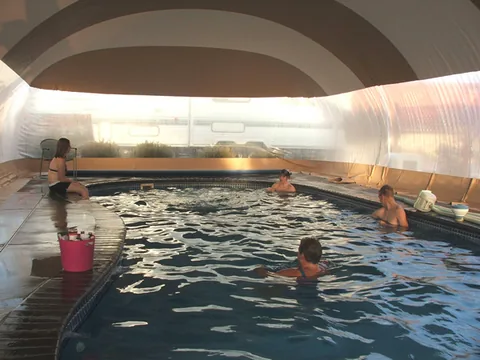 Four people swimming beneath a tan and white striped pool dome