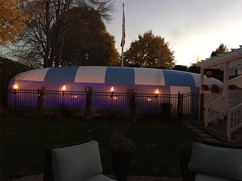 Blue and white pool dome glowing behind a fence at dusk