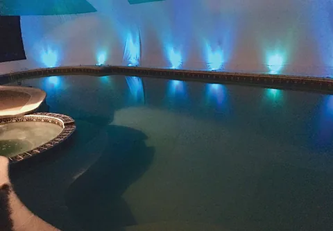 Blue-lit freeform pool and hot tub inside an aqua and white dome at night