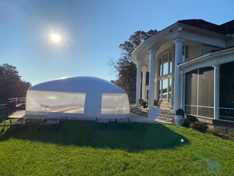 Sunlit pool dome on a lawn beside a home