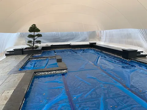 Interior view of a free-form pool with a blue pool cover under the dome