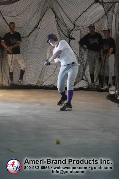Baseball player preparing to hit a ball inside a netted pitching dome