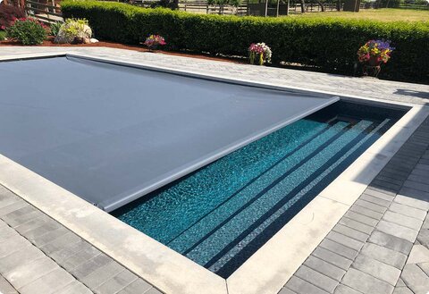 Gray automatic pool-cover fabric partially extended over a rectangular pool