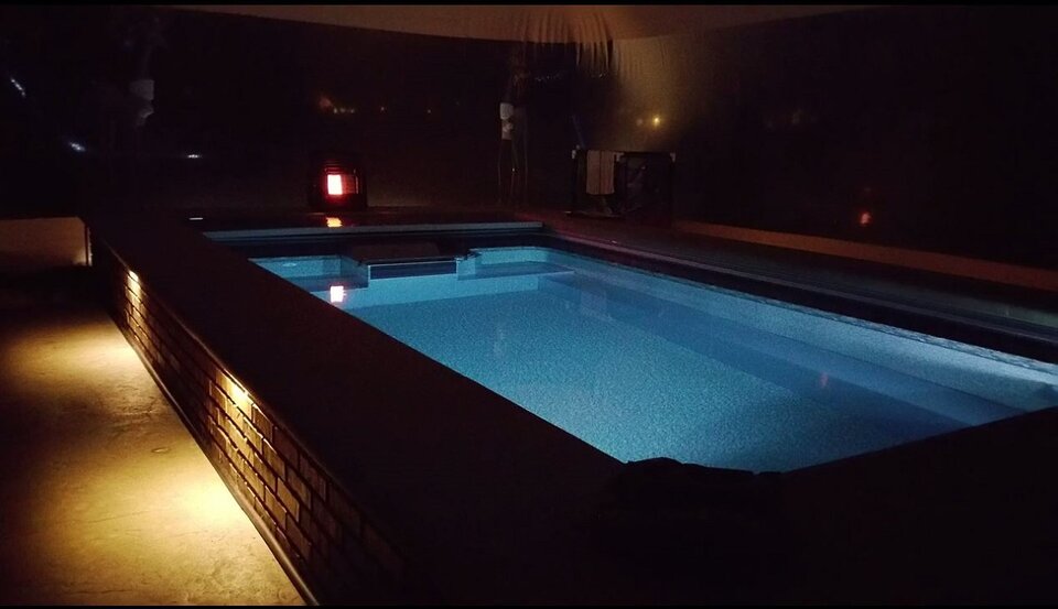 Illuminated swim spa and patio inside the clear-walled enclosure after dark