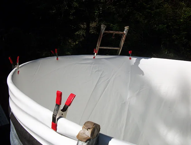 White liner opened inside a corrugated metal tank, its top edge folded over the rim and held temporarily with red clamps