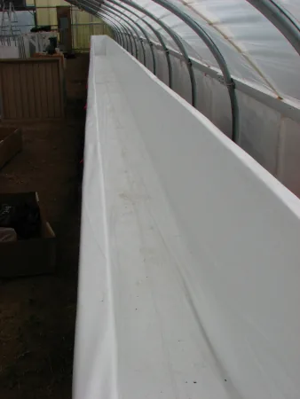 White hydroponic tank liner installed along a greenhouse wall
